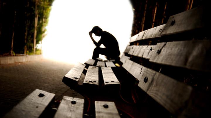 Silhouette of person with head in hands on park bench