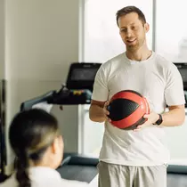 Therapist holds medicine ball and talks to a woman. 